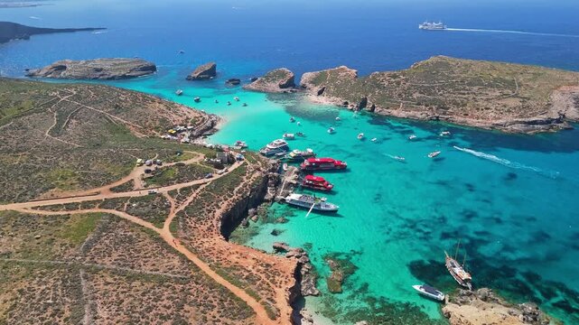 Blue Lagoon, Comino, Malta, features turquoise crystal-clear waters, rocky shores, and anchored boats between Comino and Cominotto, viewed from above on a sunny Mediterranean day.