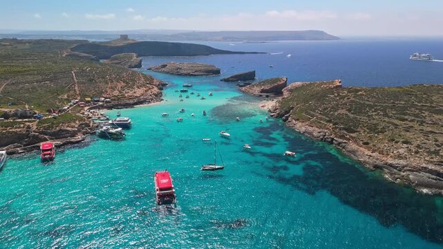 Blue Lagoon, Comino, Malta, and nearby Cominotto islands are surrounded by turquoise, crystal-clear Mediterranean waters, boats, and rocky coastline in this tranquil drone view on a sunny spring day.