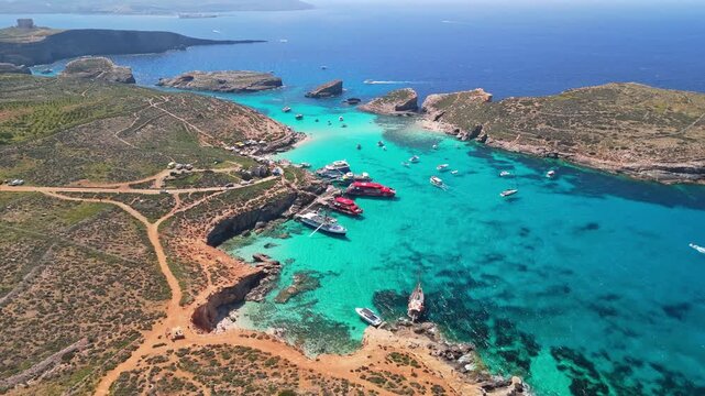 Blue Lagoon, Comino, Malta, features crystal-clear turquoise waters, rocky shores, anchored boats, and nearby Cominotto island along the Mediterranean coastline in a tranquil drone view.