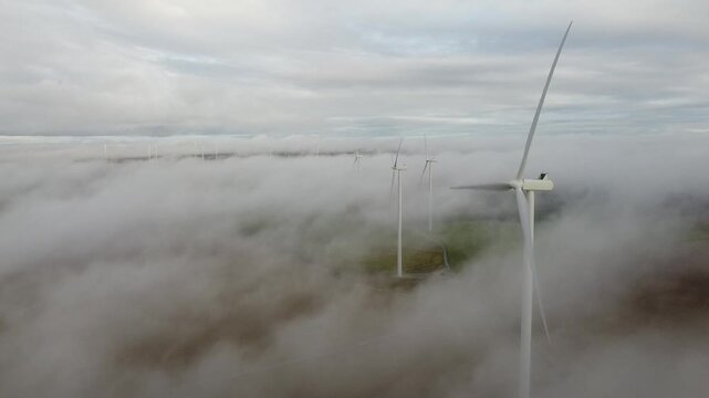 Wind turbines operating in low cloud cover above foggy terrain with misty hills