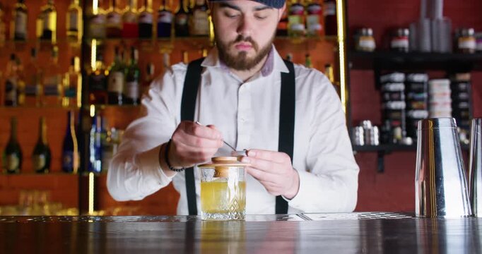 Flair bartending. Alcohol beverage. Skillful male barman making drink in glass using liquid decoration flaming tool at bar counter.