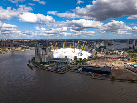 Aerial view of The O2 arena on the Greenwich Peninsula surrounded by the River Thames and modern skyscrapers under a cloudy sky London, England, United Kingdom.