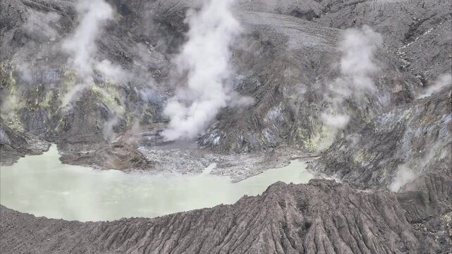 Wide shot of Tangkuban Perahu crater with white sulfur gas and rocky terrain. Exotic volcanic landscape for travel and education content.