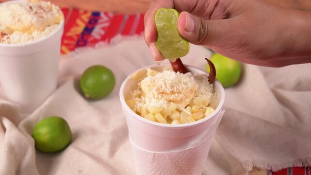 A woman's hand squeezes the juice of a lemon onto Mexican street corn in a cup