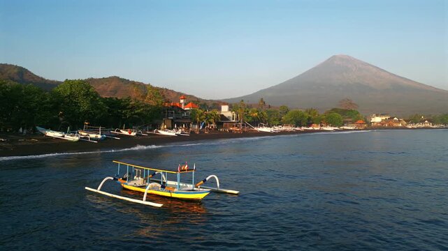 Traditional boat in the ocean near black sand Amed Beach with Mount Agung in Bali. Beautiful tropical coast at sunset