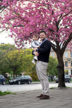 Father holding baby under pink cherry blossoms in spring Vyshyvanka