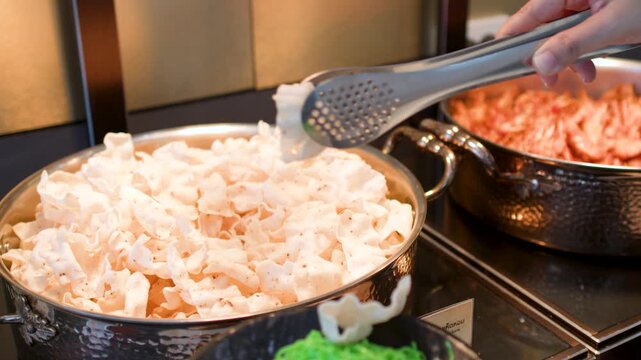 Person Using Metal Tongs to Serve Shrimp Crackers at Buffet
