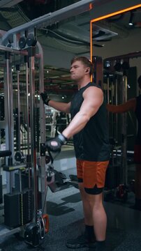 Vertical Muscular Caucasian man in his 30s performs single-arm cable lateral raise targeting side deltoid muscles on functional trainer in modern gym