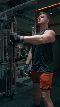 Muscular Caucasian man in his 30s performs single-arm cable rear delt pull targeting posterior deltoid muscles on functional trainer in modern gym