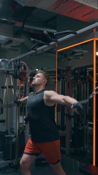 Side view of fit athlete performing low cable flyes on crossover machine for chest pectoral muscle development in dark modern fitness center with industrial interior