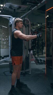 Athletic Caucasian man in his 30s performs alternating single-arm cable rear delt pull-aparts targeting posterior deltoid muscles on functional trainer - vertical cinematic shot