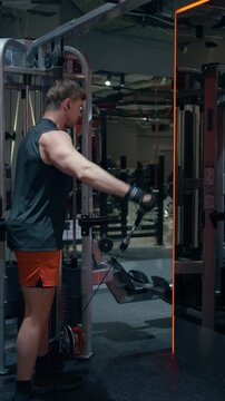 Caucasian man in his 30s performs cable lateral raise targeting side deltoid muscles on functional trainer indark gym looking at mirrow