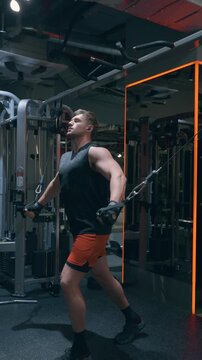 Athletic Caucasian man in his 30s performs low cable chest fly on crossover machine targeting lower pectoral muscles in dark modern gym