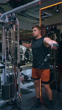 Athletic Caucasian man with big arms performs single-arm cable lateral raise targeting side deltoid muscles on a functional trainer in a modern gym