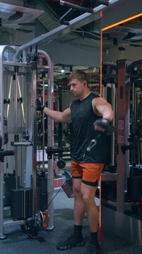 Muscular Caucasian man in his 30s performs cable lateral raise targeting side deltoid muscles on functional trainer in modern gym