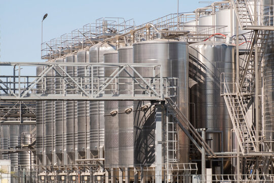 Steel tanks stand in a large industrial site with clear blue sky above and metal structures around them