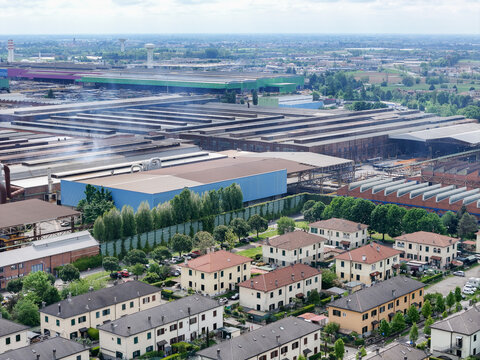 Aerial view of the large industrial complex and residential houses surrounded by green trees and flat landscape Dalmine, Lombardy, Italy.