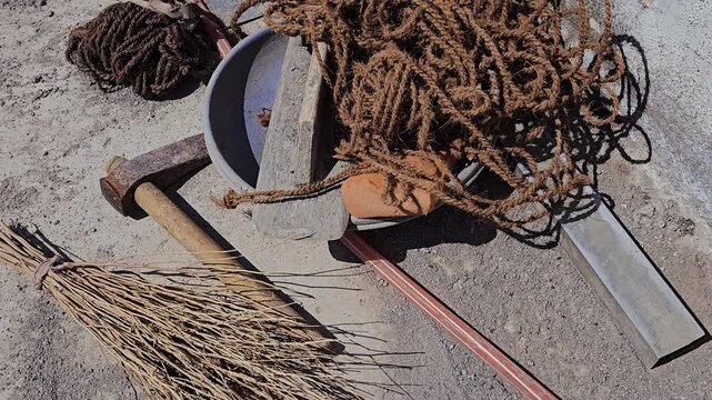 Tools for the trade: a shovel, mixing bowl, leveler, & hammer chisel axe lie scattered near coco coir rope. This sturdy fiber binds bamboo framing for work stands, essential for traditional plastering