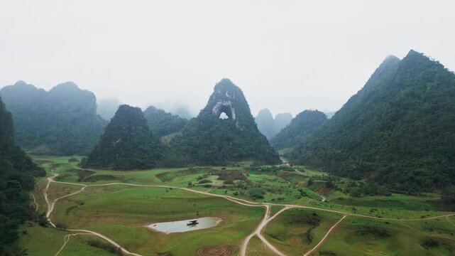 Limestone karst mountain with natural rock arch partially obscured by dense fog and light rain creating dark moody atmosphere in low visibility aerial drone view at Gods Eye Mountain Vietnam