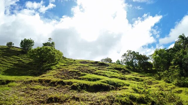 Sunlit Grassy Ridge On Siquijor With Small Lookout Hut, Vibrant Blue Sky And Dramatic Clouds, Steep Slope With Tufted Grass And Scattered Trees, Warm Sunlight Casting Contrasty Shadows,
