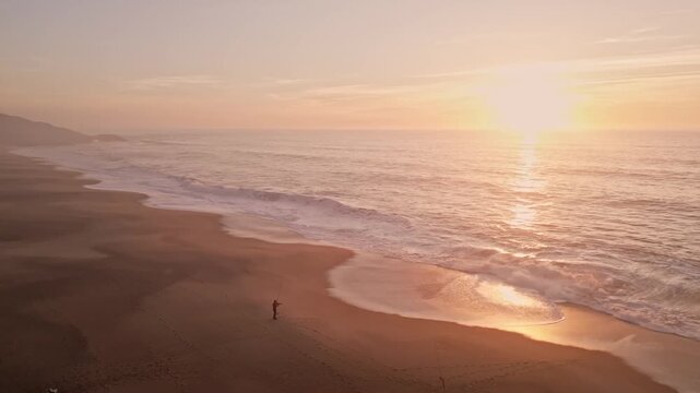 Aerial view of Praia do Salgado in Nazare at sunset. Beautiful golden waves roll onto the empty sand during the golden hour. Peaceful nature landscape for travel and meditation