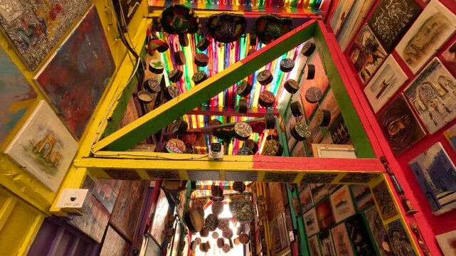 Vibrant artistic alley in Fez, Morocco filled with colorful murals, hanging textiles and handcrafted ornaments, creating an immersive cultural space with expressive street art and creative energy.