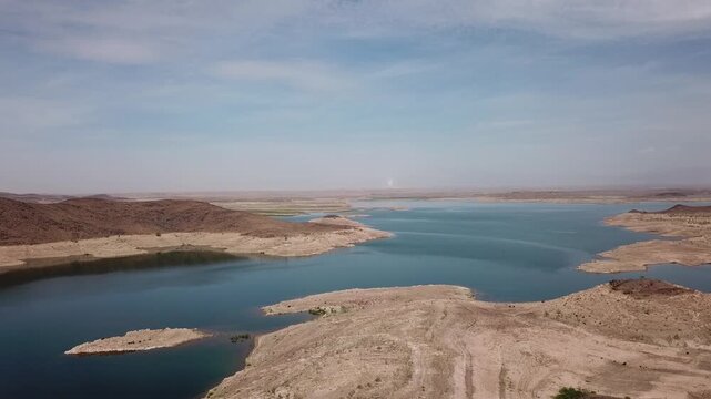 High-altitude wide drone shot showcasing the vast scale of water depletion and exposed shorelines at the El Mansour Eddahbi reservoir near Ouarzazate.
