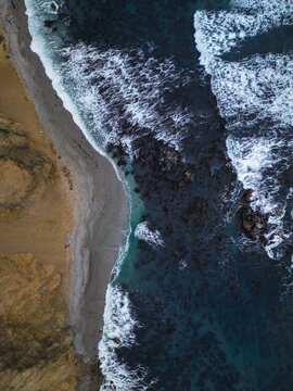 Aerial view of the Reserva Nacional de Paracas with white waves crashing against the sandy shore and rugged cliffs in Paracas, Ica, Peru.