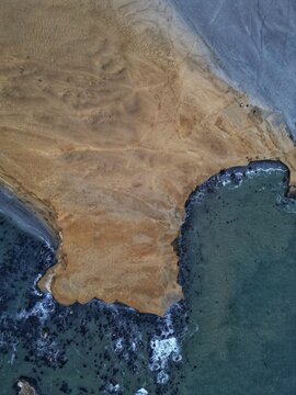Aerial view of the rugged desert coastline of Reserva Nacional de Paracas with golden cliffs meeting the turquoise ocean waves Paracas, Ica, Peru.