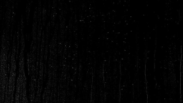 Close-up drops of water sliding down on the glass surface over black background.