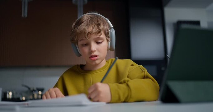 Young Student Practicing Handwriting Quietly. Male Student Reviewing Notes With Headphones Nearby