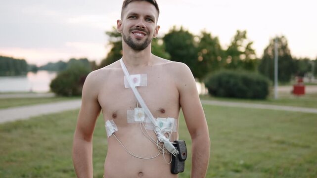 Portrait of man during heart monitoring with holter in park. Close view of sensors placed on chest area and fixed on body with patch.