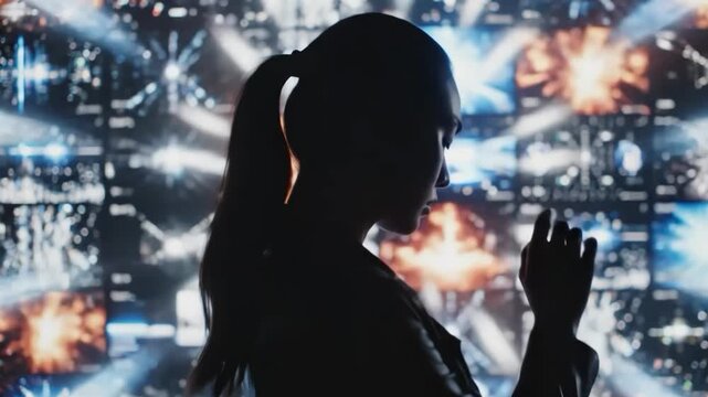 Silhouette of a woman standing in front of a wall of screens displaying colorful explosions