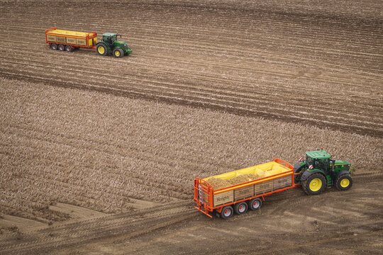 Aerial view of Keogh's Farm with green tractors and orange trailers harvesting potatoes in a vast agricultural field in Oldtown, County Dublin, Ireland.