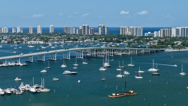 Aerial view of Peanut Island and the Blue Heron Bridge with numerous boats anchored in the turquoise water and the coastal skyline Palm Beach County, Florida, United States.