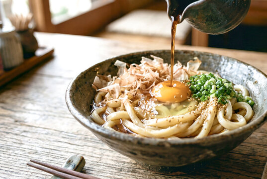 卵と鰹節のぶっかけうどんにだしを注ぐ