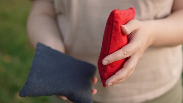 Woman touching blue and red bean bags for cornhole game, closeup. Person evaluating weight and quality of material of sports equipment for popular American game. Bean bags size 6 inches.