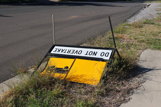 Do Not Overtake traffic warning sign tipped over and lying flat on a grassy roadside verge