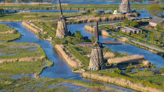 Aerial view of the historic Kinderdijk windmills standing along winding canals surrounded by lush green fields and reeds under bright sunlight Kinderdijk, South Holland, Netherlands.