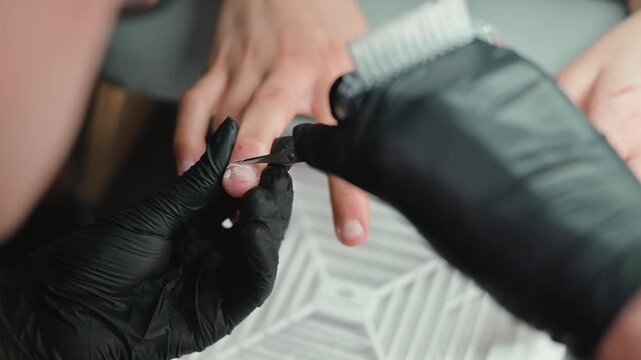 close-up view of hands receiving nail grooming. A person wears black gloves while trimming and shaping the nails, highlighting the manicure process