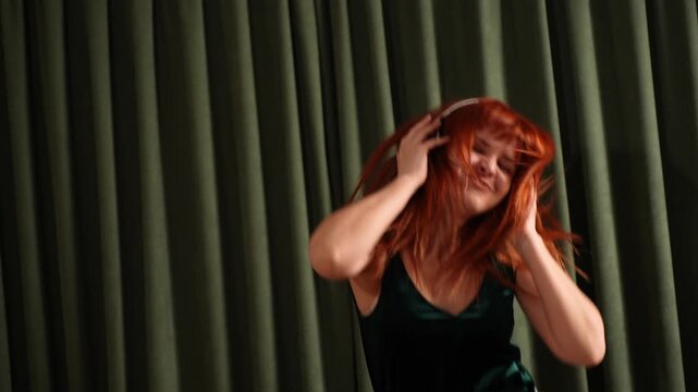 Energetic red-haired woman headbanging and listening to music in headphones, expressing raw emotion and freedom. Concepts of stress relief, music passion, joy, carefree living