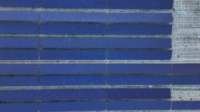 Parallel rows of solar panels form a strong geometric pattern as the camera moves laterally, revealing structured layout of a photovoltaic installation under development