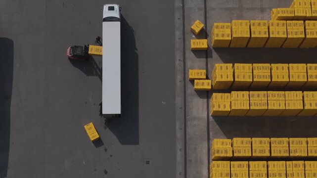 Truck and forklift operate within an organized industrial yard moving precast blocks, revealing logistics workflow and structured layout from an overhead perspective