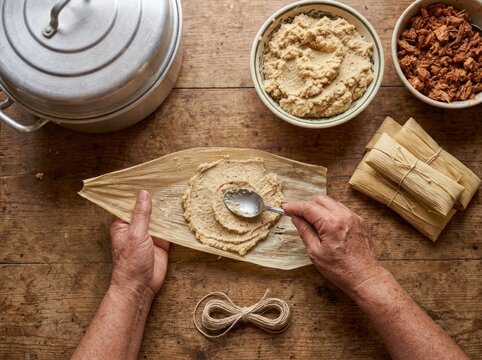 Indigenous maker spreads masa on banana leaf for traditional dish preparation in kitchen setting