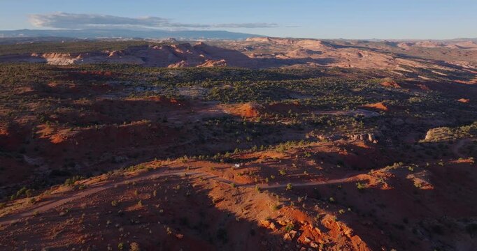 Red desert ridges and scattered juniper stretch across Grand Staircase Escalante landscape at sunset, drone establishing backdrop