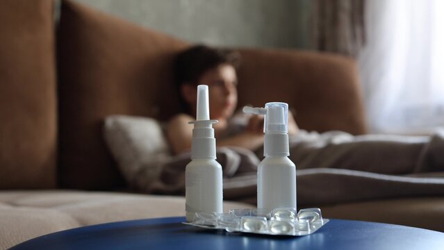 sick man lying in bed suffering virus having medicine tablets. drinking pill. A sick teenager lies on the couch, coughing and taking pills for a seasonal virus.