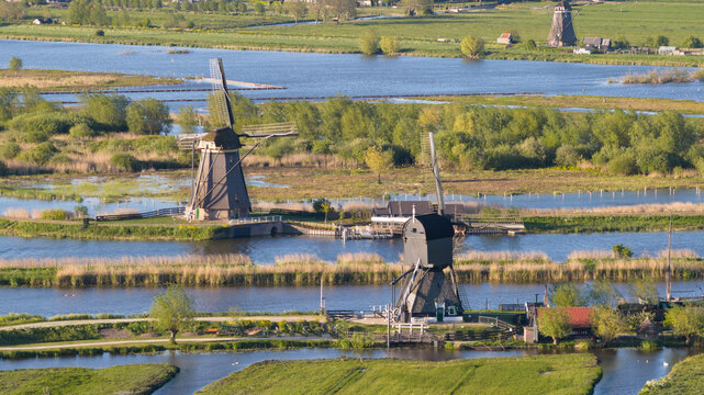 Aerial view of the historic windmills of Kinderdijk standing along the water canals surrounded by lush green polders and reeds under soft sunlight Kinderdijk, South Holland, Netherlands.