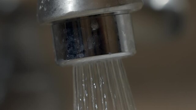 Close up of water pouring from the dirty metallic faucet in a bathroom