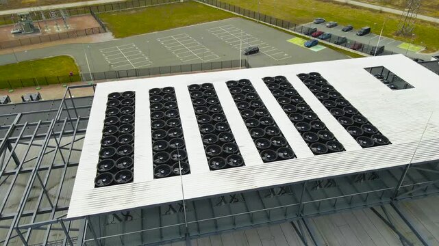 Aerial view of a large data center building rooftop with rows of industrial air conditioning fans spinning to cool the servers, highlighting modern technology and energy consumption