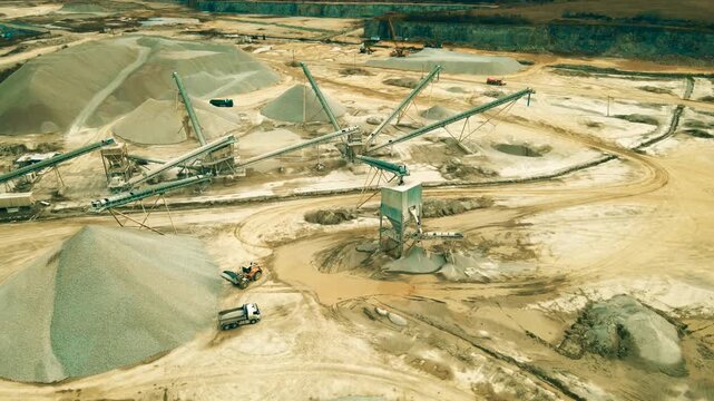 Stunning aerial perspective showing a front loader loading a dump truck at a large limestone quarry with conveyer belts, aggregate piles, and heavy machinery for extracting minerals